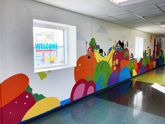 Colorful fruit and vegetables painted in a long hallway creating a large scale mural of the city of Houston to welcome staff and guests of the Houston Food Bank.