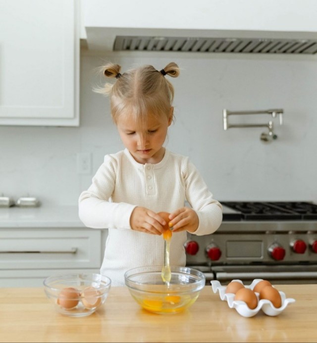 A child cracking eggs into a glass bowl