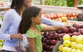 A mother and daughter overlook the fresh apple display in their local grocery store both choosing ripe, red apples.