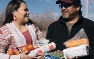 A couple seeking help have their arms full of nutritious foods while smiling at each other.