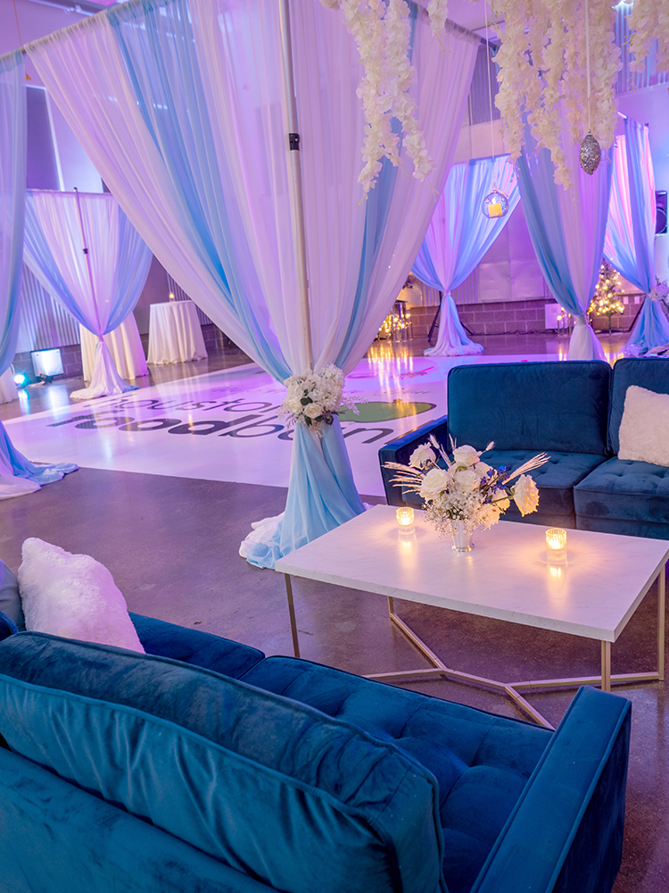A decadent setup in Houston Food Bank's Conference Center complete with lush, blue couches between a white candle-lit table and a sheer curtain encased dancefloor in the background.