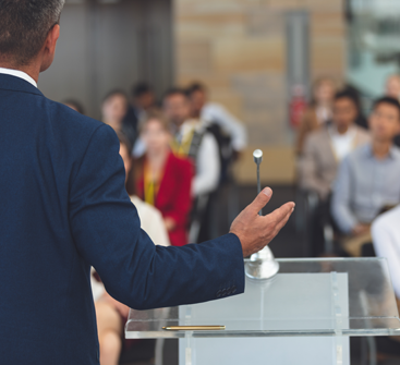 Rear view of politician standing at podium addressing a room of citizens