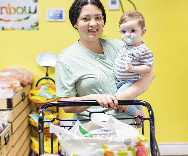 A young mother and her baby with a cart full of groceries.