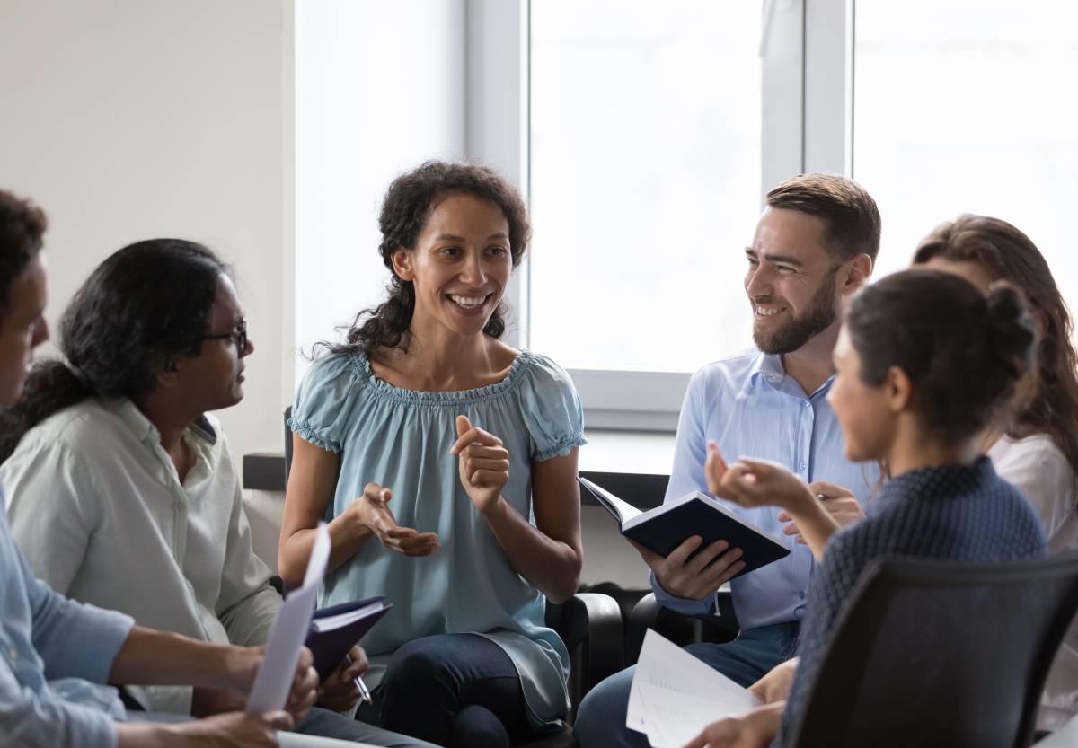 Diverse group sitting in a circle, actively discussing while one woman speaks and others listen and smile