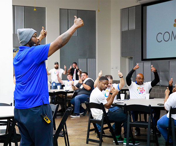 PullUpAChair 600×500 1 A Houston Food Bank employee and seated volunteers give a thumbs up.