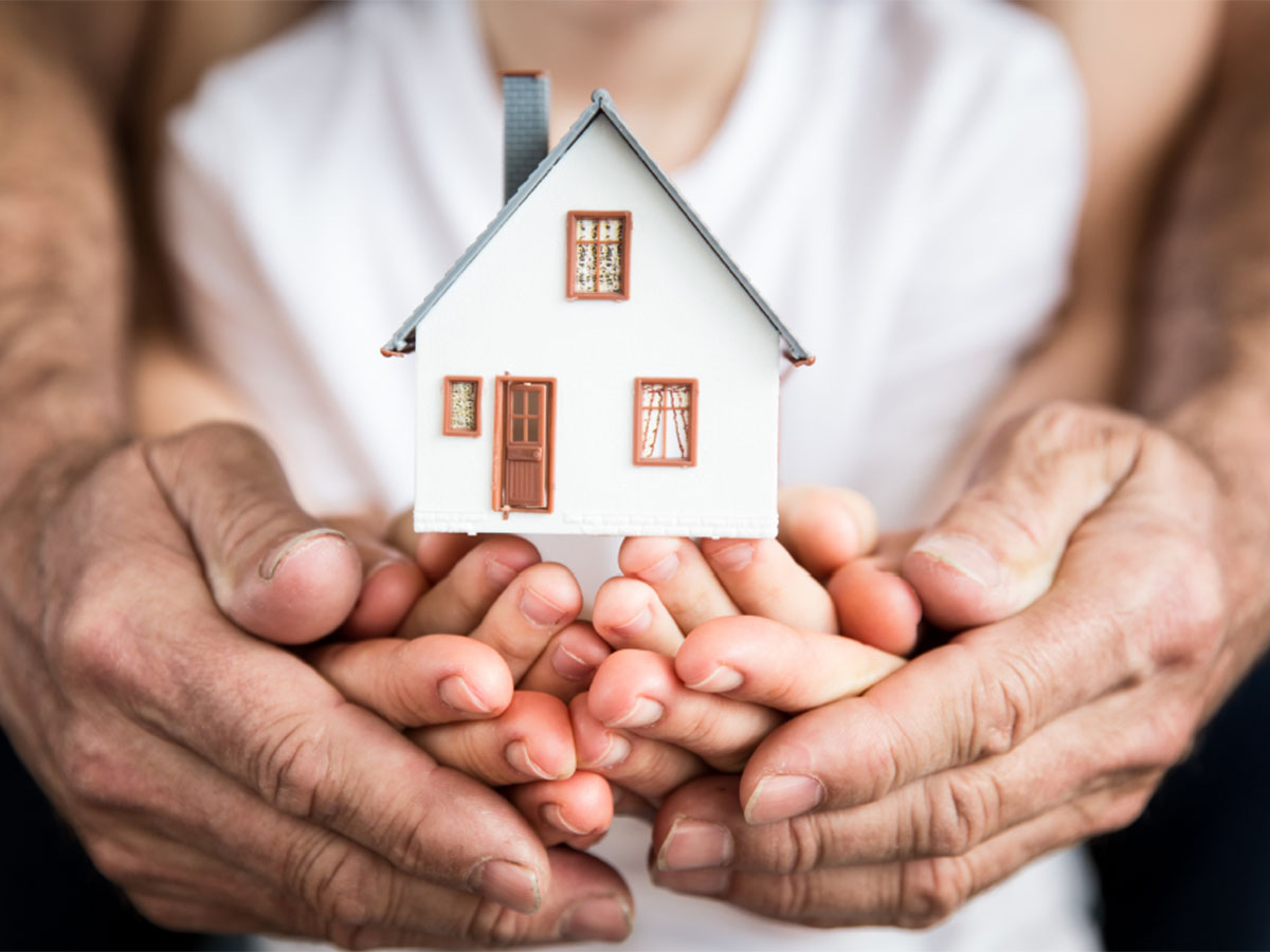 Multigenerational hands holding a model house.