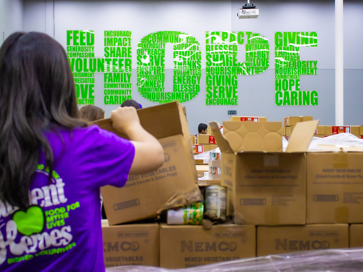 A volunteer packs food boxes in front of a wall with HOPE written on it.